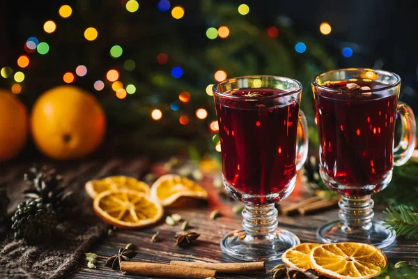 Vino caliente en copas de cristal con naranja, canela, cardamomo, un anís estrellas en la mesa decorado con un árbol de Navidad y una guirnalda — Foto de Stock