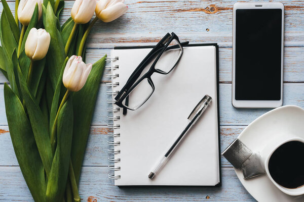 White bouquet of tulips on wooden background with coffee Cup, smartphone and empty notebook