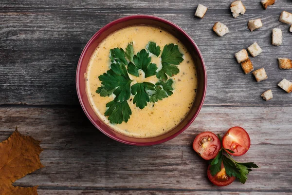 Kürbiscremesuppe in Schüssel mit Petersilie auf Holztisch mit Crackern und Tomaten. traditionelles Herbstfutter für Halloween — Stockfoto