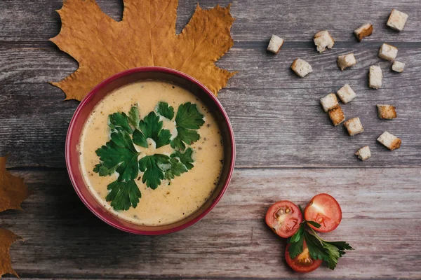 Vegetabilsk vegetarisk græskar creme suppe med persille i en skål på et træbord med tomater og kiks . - Stock-foto