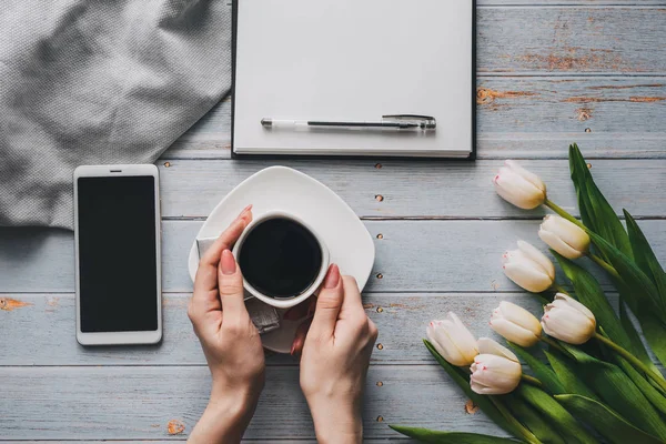 Strauß weißer Tulpen mit einer Tasse Kaffee in der Hand, einem Smartphone und einem leeren Notizbuch für den Text — Stockfoto