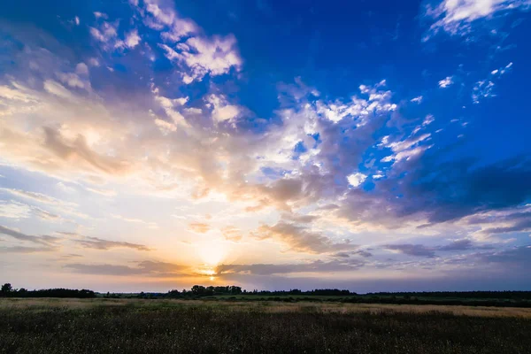 Landskap med soluppgång och sol på en molnig blå himmel över fältet på sommaren — Stockfoto