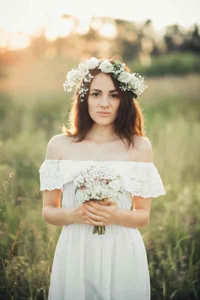 Retrato de uma menina atraente em vestido branco com um buquê de flores e uma grinalda no verão — Fotografia de Stock