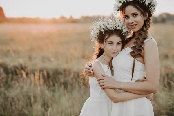 Mamma e figlia che si abbracciano insieme in abiti bianchi con trecce e ghirlande floreali in estate — Foto Stock