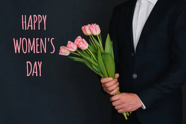 Μπουκέτο ροζ λουλούδια από τουλίπες στα χέρια των ανδρών. Ευχετήρια κάρτα με την επιγραφή χαρούμενη μέρα των γυναικών — Φωτογραφία Αρχείου