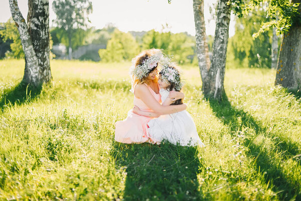 mom hugs her daughter sitting on the grass outdoors on a Sunny summer