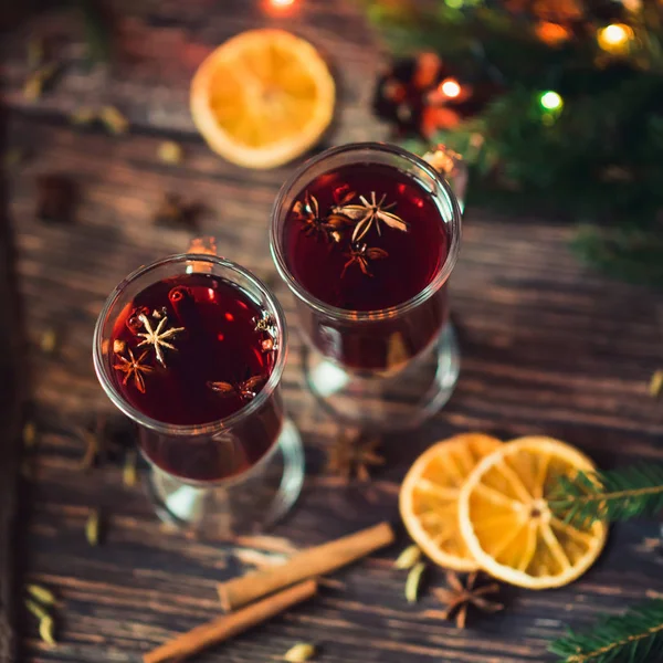 Dwie szklanki z grzanym winem, na drewnianym stole z pomarańcza, cynamon, kardamon, gwiazdki anyżu. Tradycyjne zima gorący napój alkoholowy — Zdjęcie stockowe