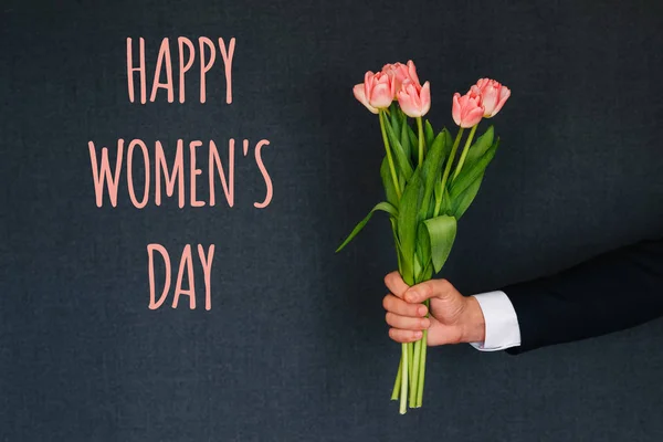 Strauß rosa Tulpen in der Hand eines Mannes. Glückwunschkarte mit Text zum Frauentag — Stockfoto