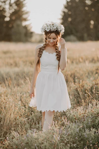 夏のフィールドで花の花輪と三つ編みを持つ白いドレスの女の子 — ストック写真