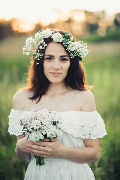 Retrato de uma menina atraente em vestido branco com um buquê de flores e uma grinalda no verão — Fotografia de Stock