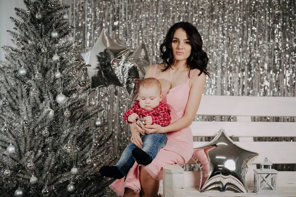 Молодая мама с новорожденным сыном сидит на фоне рождественского декора — стоковое фото