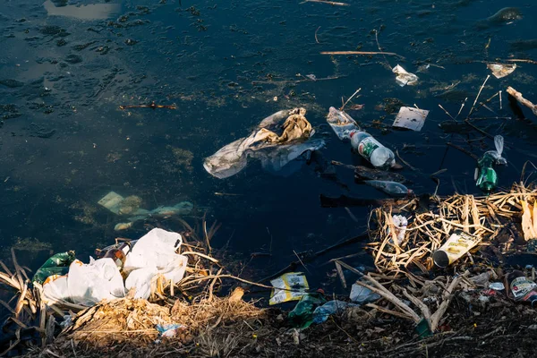 VICHUGA, RÚSSIA - ABRIL 21, 2019: Vários lixo e lixo de garrafas de plástico e sacos na água e na margem do rio — Fotografia de Stock