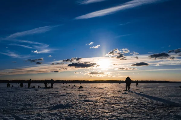 Winter fishing. Silhouette of fishermen catching fish on the icy surface of the river