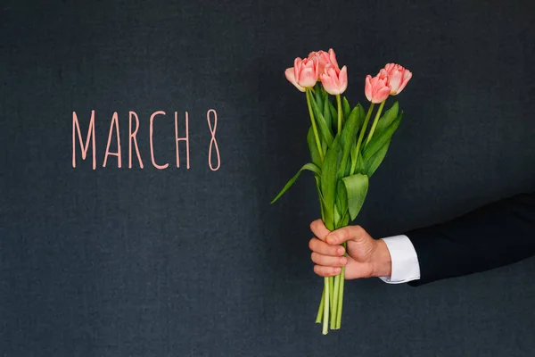 Ramo de tulipanes rosados en la mano de un hombre. Tarjeta de felicitación con texto 8 de marzo — Foto de Stock