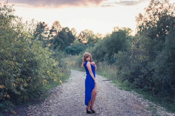 Chica en vestido azul posando sobre un fondo de puesta de sol — Foto de Stock