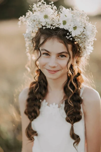 Portret uśmiechniętej młodej dziewczyny w białej sukni i kwiatowy wieniec na włosach z warkocze w polu letnim — Zdjęcie stockowe