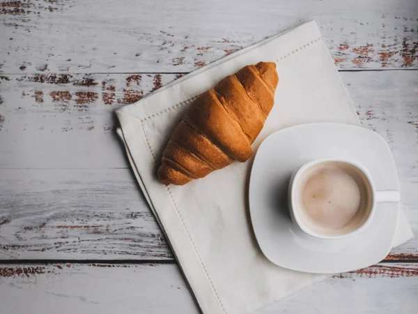 Kaffee und ein Croissant auf einem Holztisch. traditionelles französisches Abendessen am Morgen. — Stockfoto