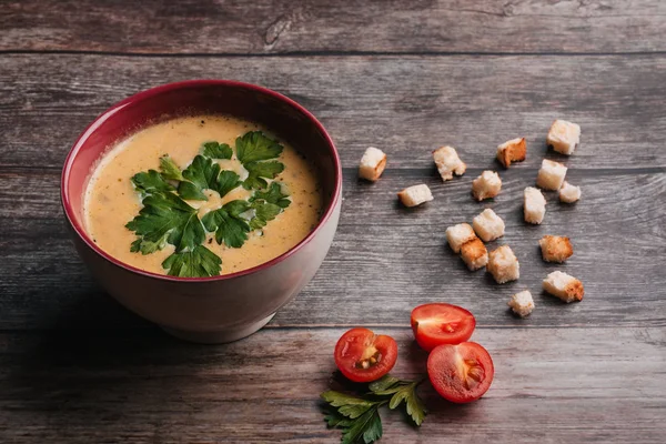 Kürbiscremesuppe in Schüssel mit Petersilie auf Holztisch mit Crackern und Tomaten. traditionelles Herbstfutter für Halloween — Stockfoto