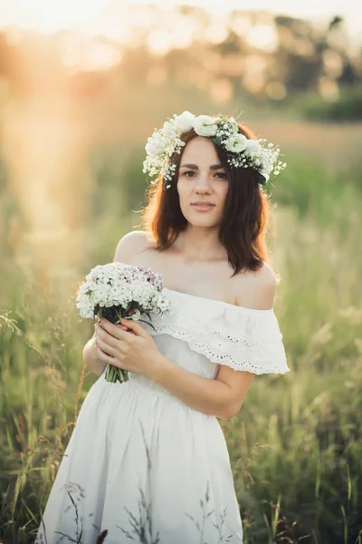 Piękna młoda dziewczyna z bukietem kwiatów i wieniec w białej sukni — Zdjęcie stockowe