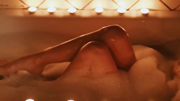 Meztelen barna lány szexuálisan megcirógatja lábát, és élvezi a fürdőszobában hab egy pohár pezsgő — Stock videók