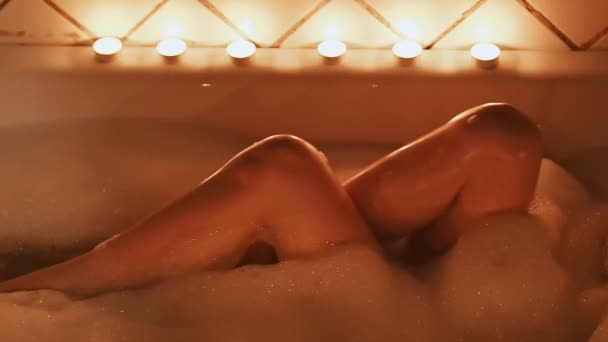 Обнаженная брюнетка сексуально ласкает ноги и наслаждается в ванной с пеной с бокалом шампанского — стоковое видео