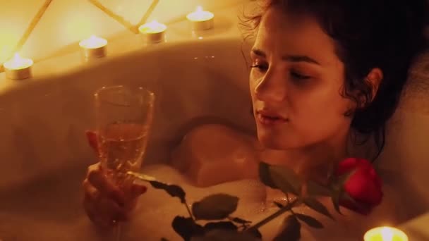 Fericit frumoasă fată tânără întinsă în baie cu spumă cu un trandafir în mână și băut șampanie — Videoclip de stoc