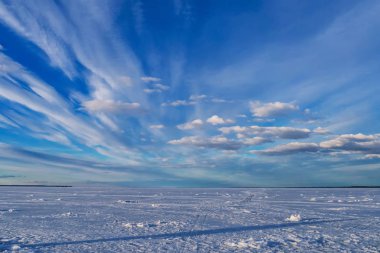 Kış manzarası, buzlu nehir, mavi gökyüzü ve beyaz bulutlar.