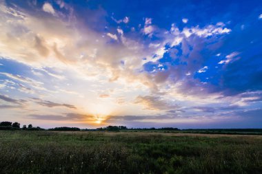 yaz aylarında alan üzerinde bulutlu bir mavi gökyüzünde gün doğumu ve güneş ile manzara