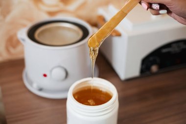 bir kavanozda depilasyon için doğal sıcak şeker ezmesi ve bir kadın güzellik elinde ahşap bir spatula üzerinde