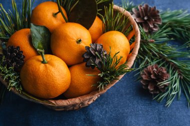 Çam dallarıyla süslenmiş ahşap bir sepette mandalinalar.