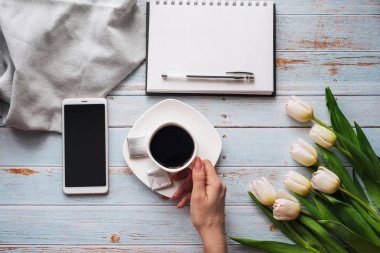 kadınların elinde bir fincan kahve ile beyaz lale buketi, bir akıllı telefon ve metin için boş bir dizüstü bilgisayar