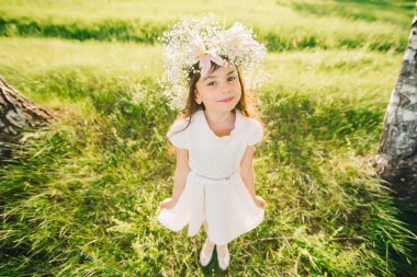 mutlu genç kız bir çelenk çiçek kafasını ve mutlu bir şekilde gülümseyerek beyaz bir elbise ile