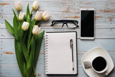 Lale kahve fincanı, smartphone ve boş defter ile ahşap arka plan üzerinde beyaz buket