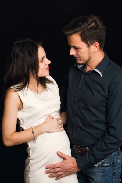 Ευτυχισμένη έγκυος σύζυγος και ο σύζυγος αγκαλιάζει σε μαύρο φόντο. Η έννοια της νεαρής οικογένειας — Φωτογραφία Αρχείου