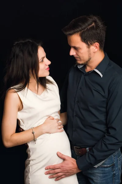 Feliz esposa embarazada y marido abrazándose en el fondo negro. El concepto de una familia joven — Foto de Stock