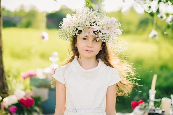 Portret van een jong meisje met een krans van bloemen op haar hoofd op een weide — Stockfoto