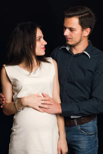 Feliz esposa embarazada y marido abrazándose en el fondo negro. El concepto de una familia joven — Foto de Stock