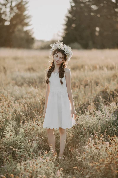 Jong meisje in een witte jurk en een bloem krans in de zomer in het veld — Stockfoto