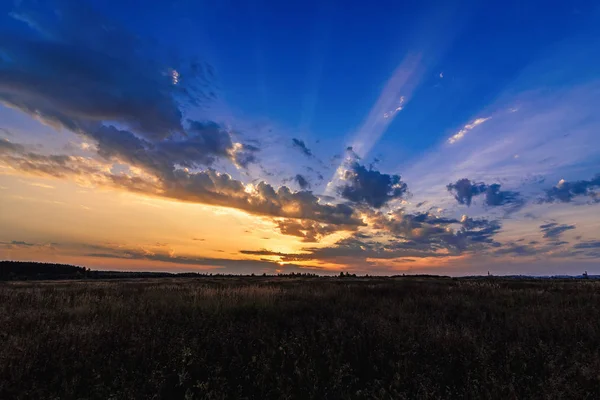 Orange Blå solnedgång med solstrålar genom molnen i himlen på fältet på kvällen — Stockfoto