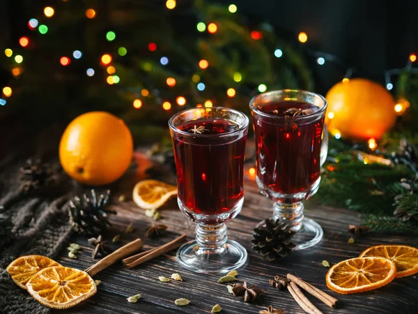 Δύο ποτήρια με mulled κρασί σε ένα ξύλινο τραπέζι με πορτοκάλι, κανέλα, κάρδαμο, γλυκάνισο αστεριών. Παραδοσιακό χειμώνα ζεστό αλκοολούχο ποτό — Φωτογραφία Αρχείου