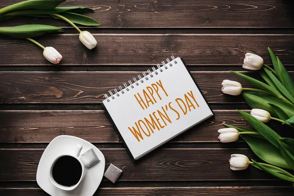 Witte Tulp bloemen met een kopje koffie op een houten tafel. Wenskaart met opschrift Happy Women 's Day — Stockfoto