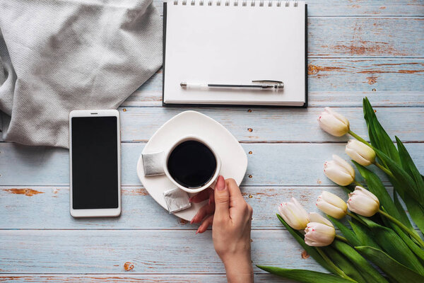 bouquet of white tulips with a Cup of coffee in women's hands, a smartphone and an empty notebook for text