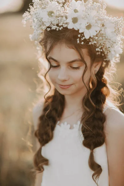 Πορτρέτο ένα νεαρό κορίτσι με ένα λευκό φόρεμα και ένα λουλουδάτο στεφάνι στο γήπεδο του καλοκαιριού — Φωτογραφία Αρχείου
