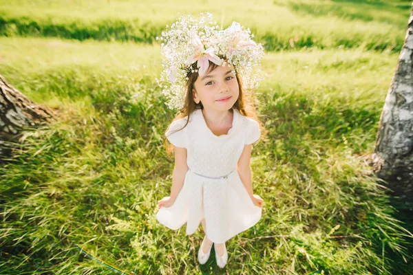 Glad ung flicka med en krans av blommor på hennes huvud och en vit klänning som ler lyckligt — Stockfoto