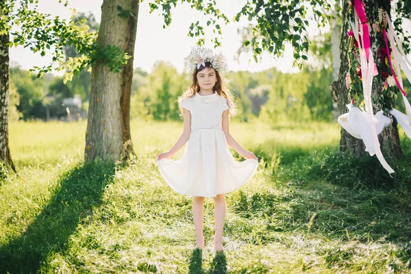Niña feliz en un vestido con una corona en la cabeza de flores en el campo — Foto de Stock
