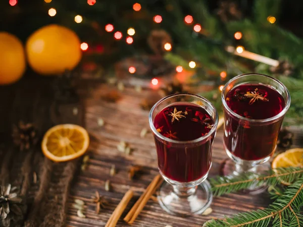 Glühwein in Glasgläsern mit Orange, Zimt, Kardamom, einem Anisstern auf dem Tisch, geschmückt mit einem Weihnachtsbaum und einer Girlande — Stockfoto