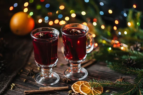 Copas con vino caliente en una mesa de madera decorada con árboles de Navidad. Bebida alcohólica tradicional de invierno con rodajas de naranja — Foto de Stock