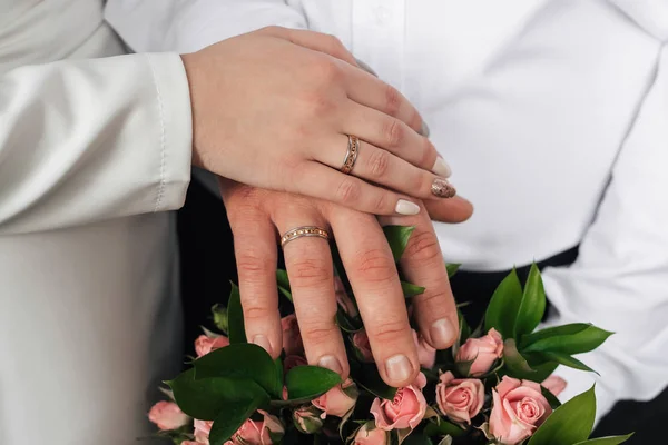 Händerna på bruden och brudgummen med guldringar på bakgrunden av bröllopsbukett — Stockfoto