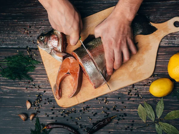 El hombre corta una trucha con un cuchillo en una tabla. Pescado crudo fresco — Foto de Stock
