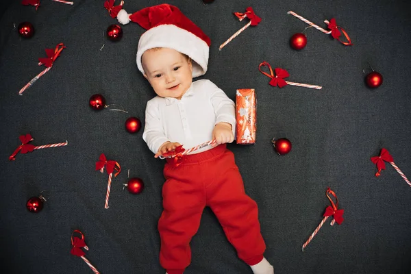 Счастливый мальчик в шляпе Санта-Клауса улыбаясь среди праздничных рождественских конфет — стоковое фото